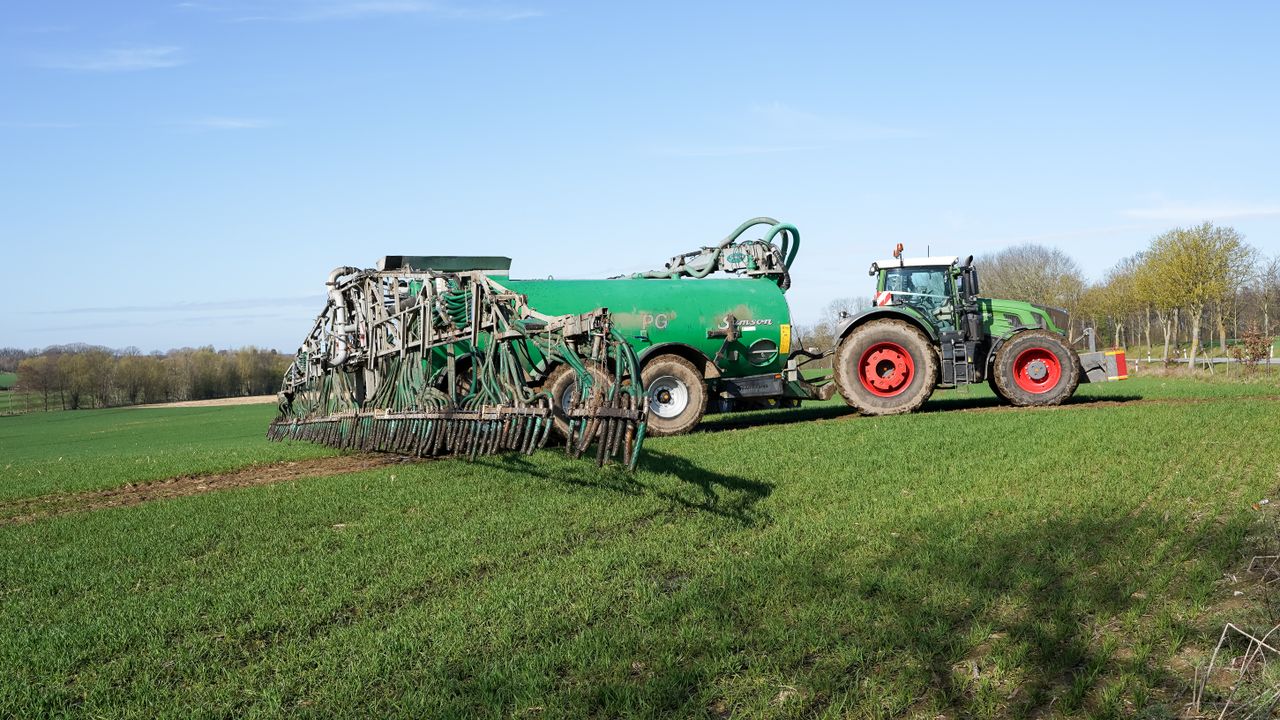 Tractor and manure spreader on green farmland in Lütau, Schleswig-Holstein, Germany.